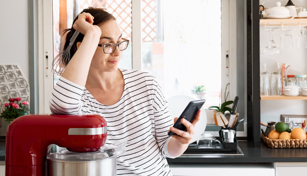 Bild på en kvinna i ett kök som läser något på sin mobiltelefon
