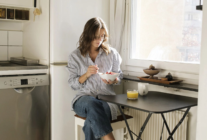 Tjej som sitter vid ett enkelt bord och &auml;ter frukost.