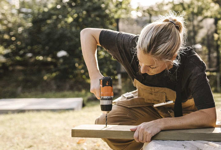 Kvinna borrar i en planka ute i trädgården.