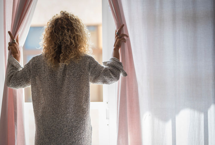 Kvinnar dra bort gardinerna f&ouml;r ett f&ouml;nster och tittar ut.