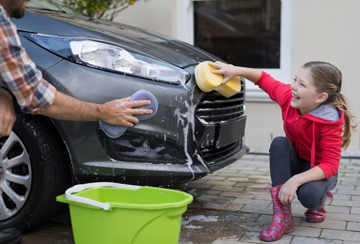 Pappa och dotter tvättar en grå bil.